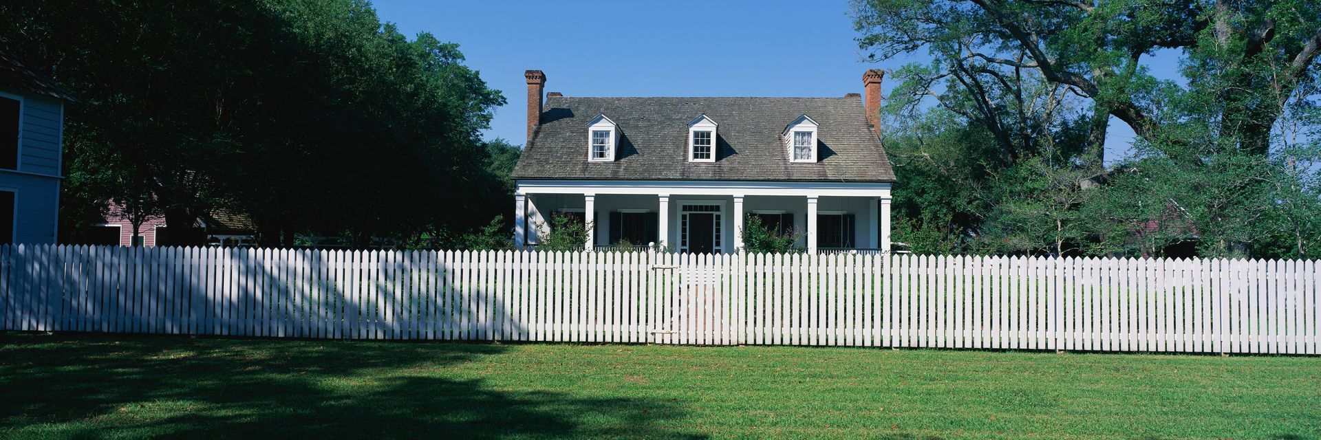 View of a house behind a white picket fence, showcasing expert new fence installation. View of a house behind a white picket fence, showcasing expert new fence installation.