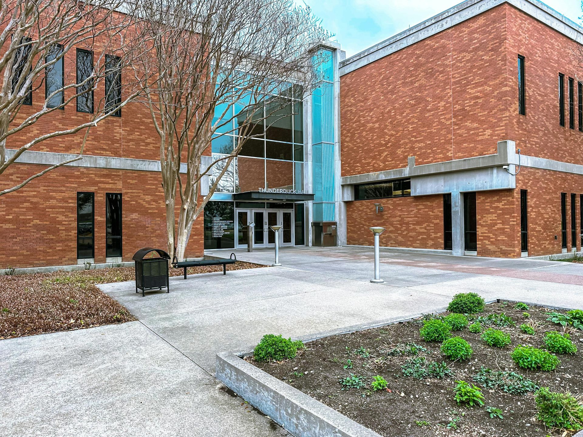Brick building with glass entrance, small courtyard, and landscaping.