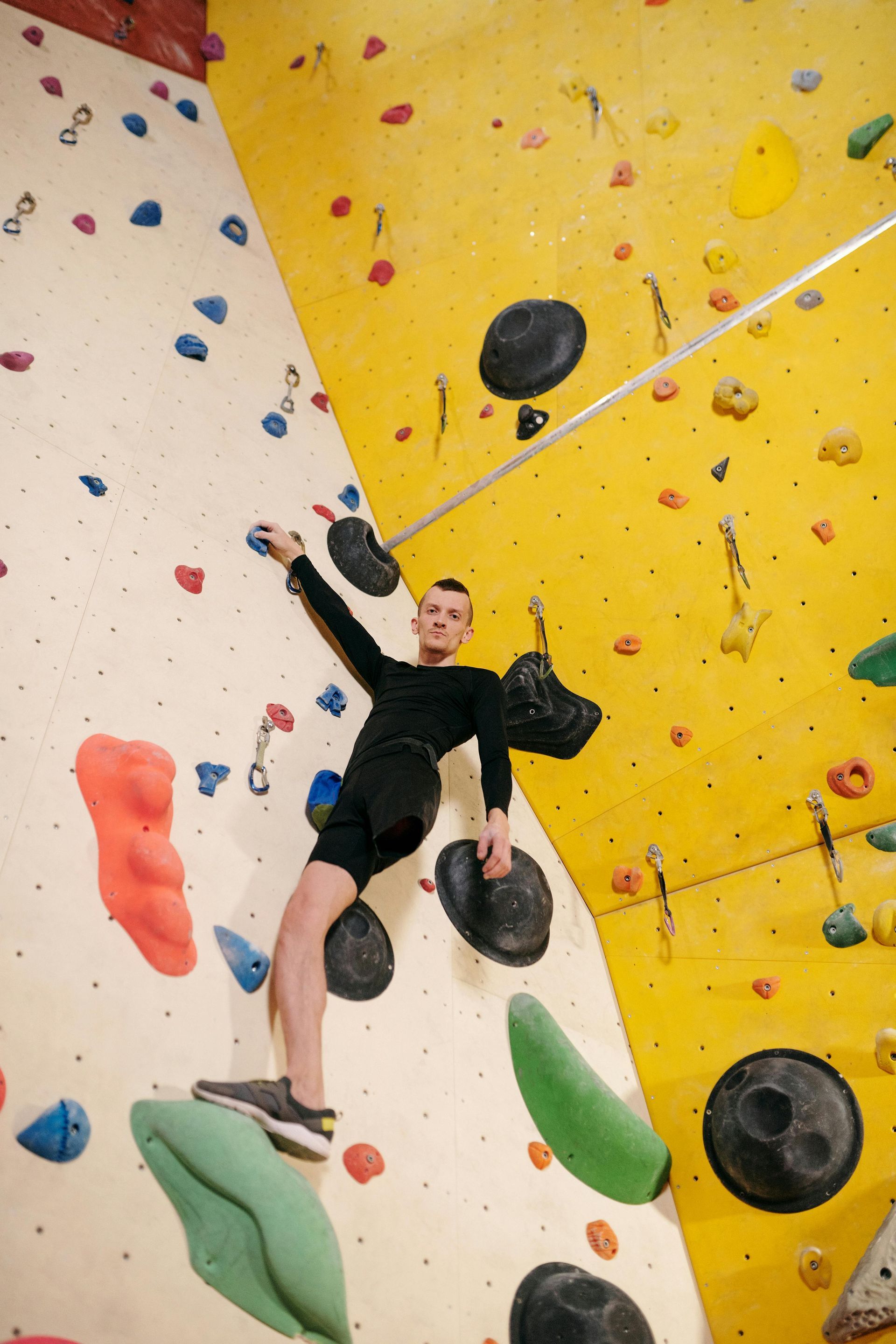 A person rock climbing on a colorful indoor wall, reaching up with one arm.