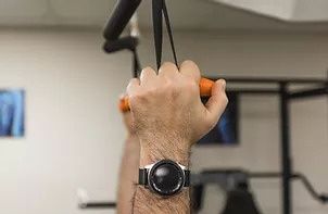A man wearing a watch is holding onto a bar in a gym.