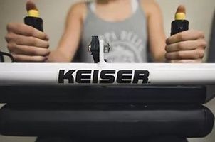 A woman is holding the handles of a keiser exercise machine.