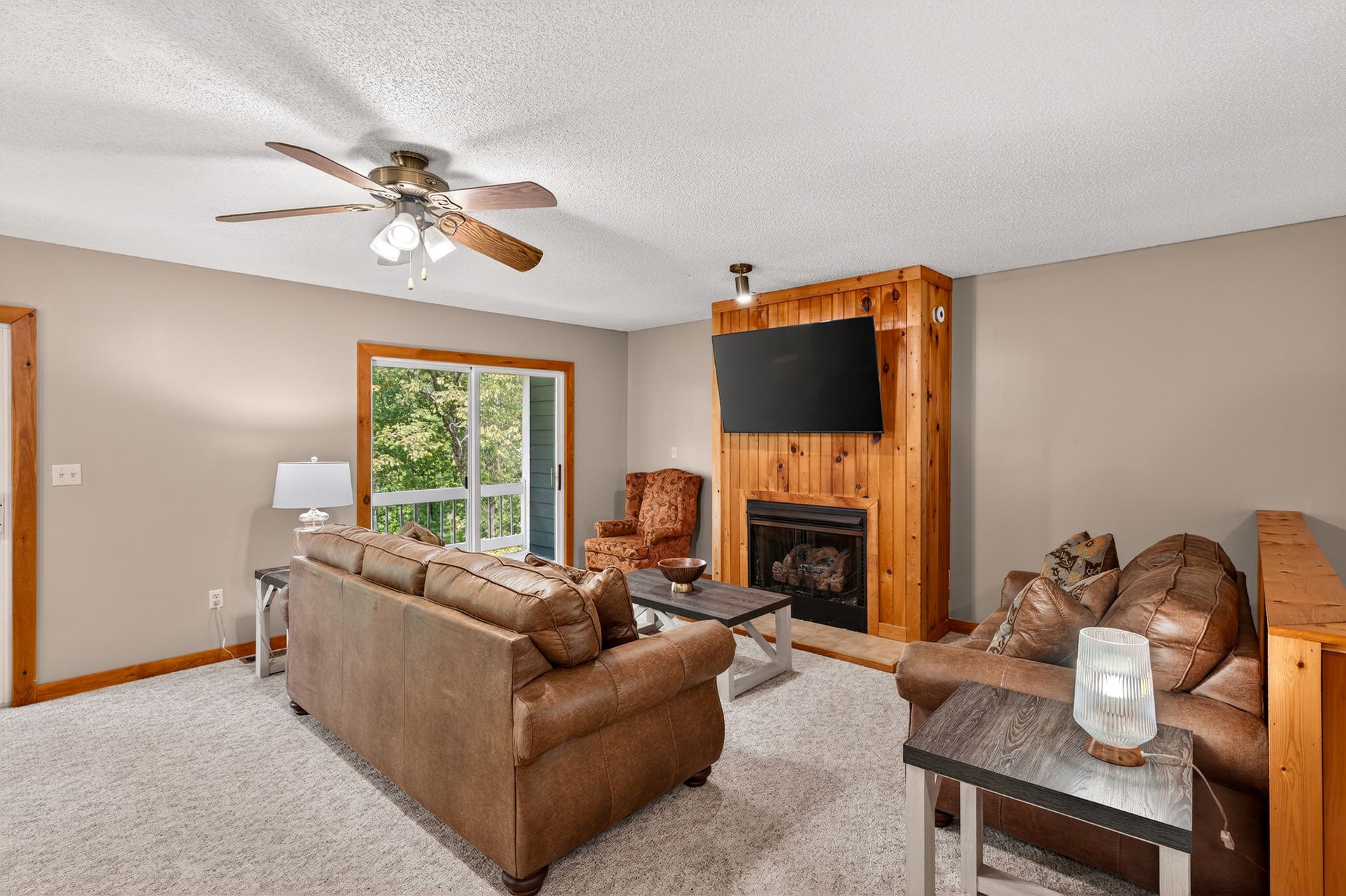 Living room with fireplace, leather furniture, sliding glass door to a deck, and beige walls.