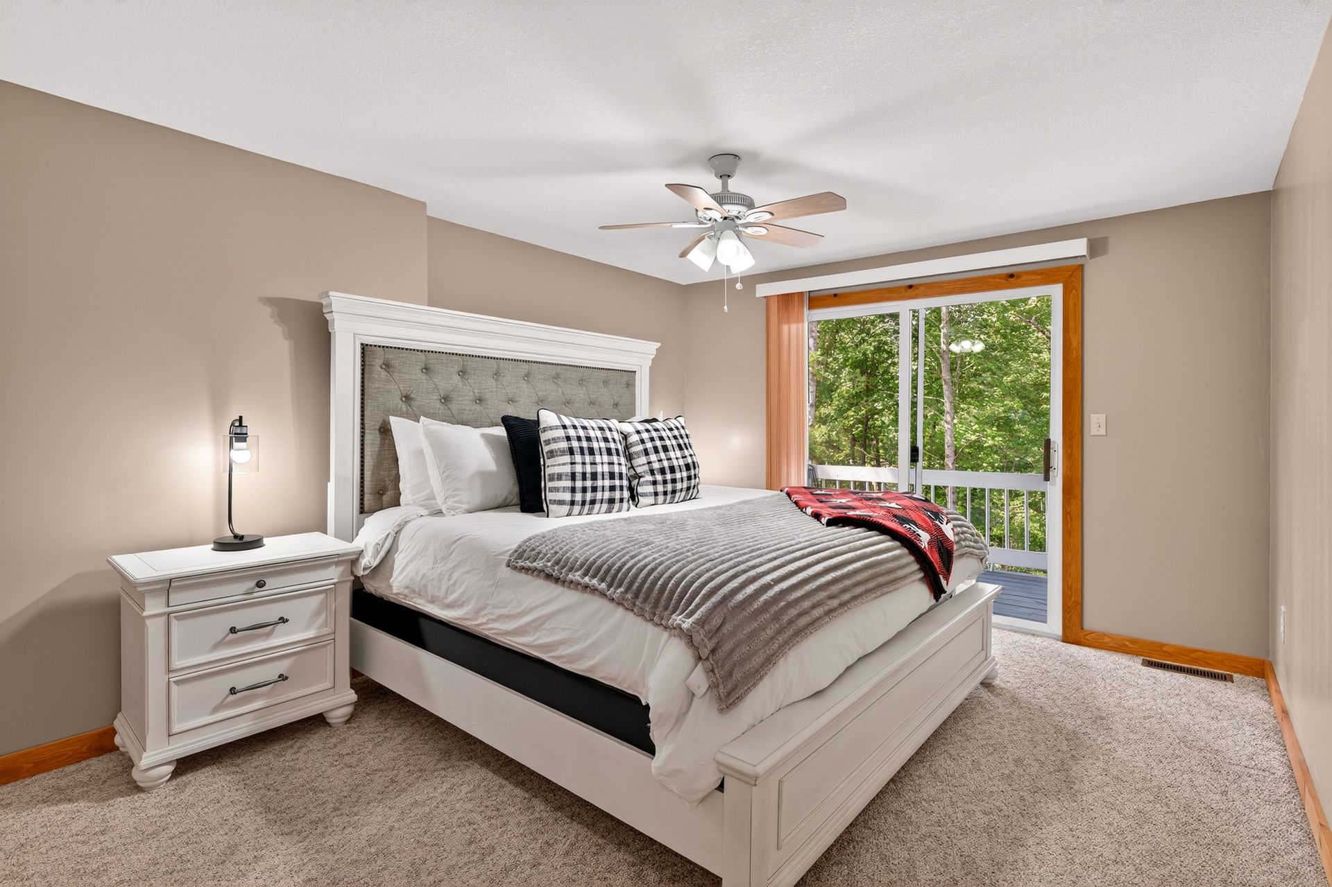 Beige bedroom with a white bed, nightstand, and sliding glass door to a deck.