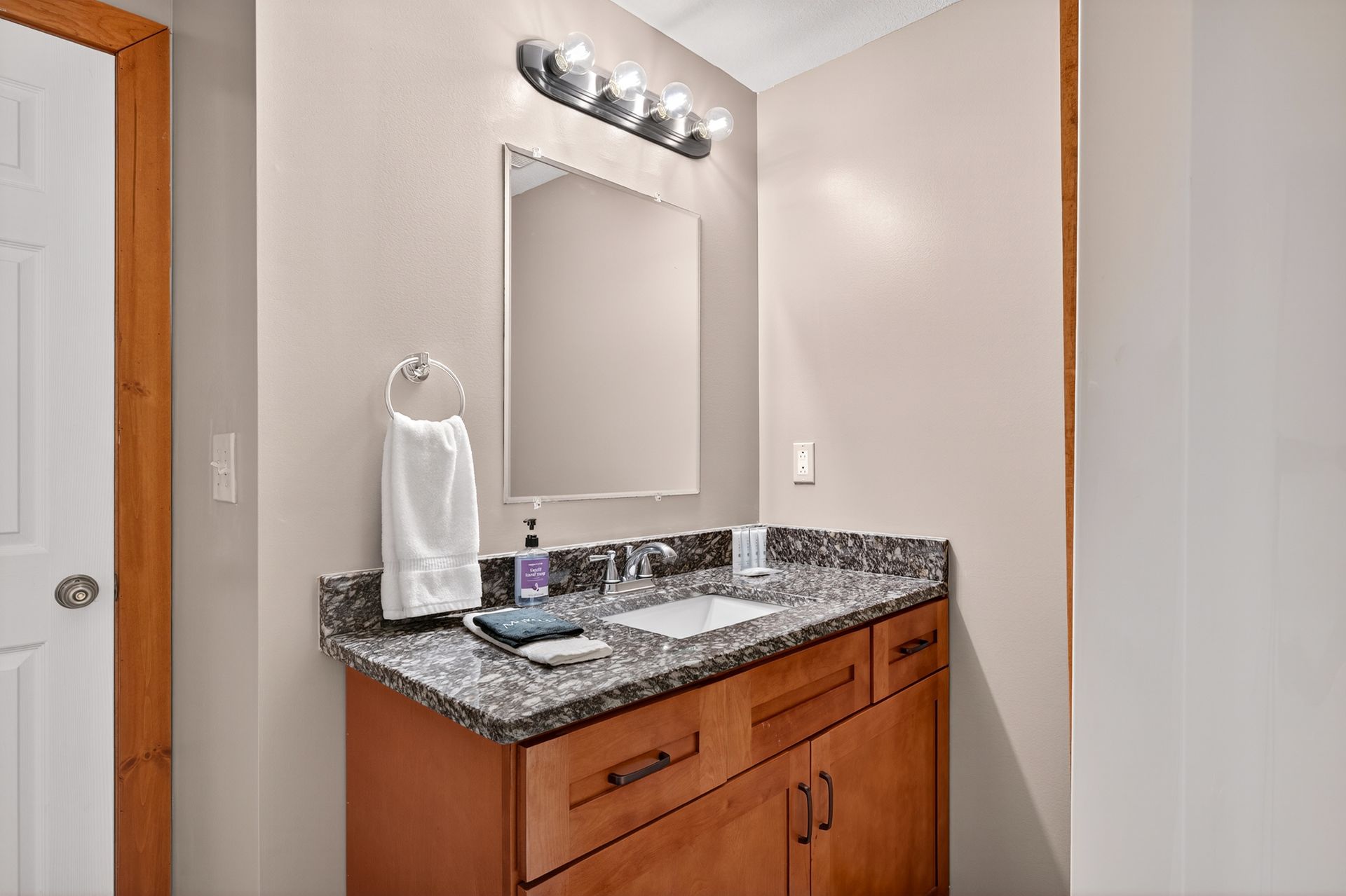 A bathroom with a vanity, mirror, and sink; beige walls, and a wooden cabinet.