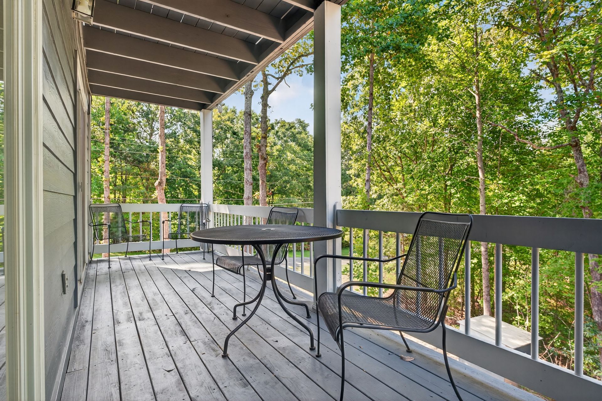 Wooden deck with black table and chairs overlooking a forest.