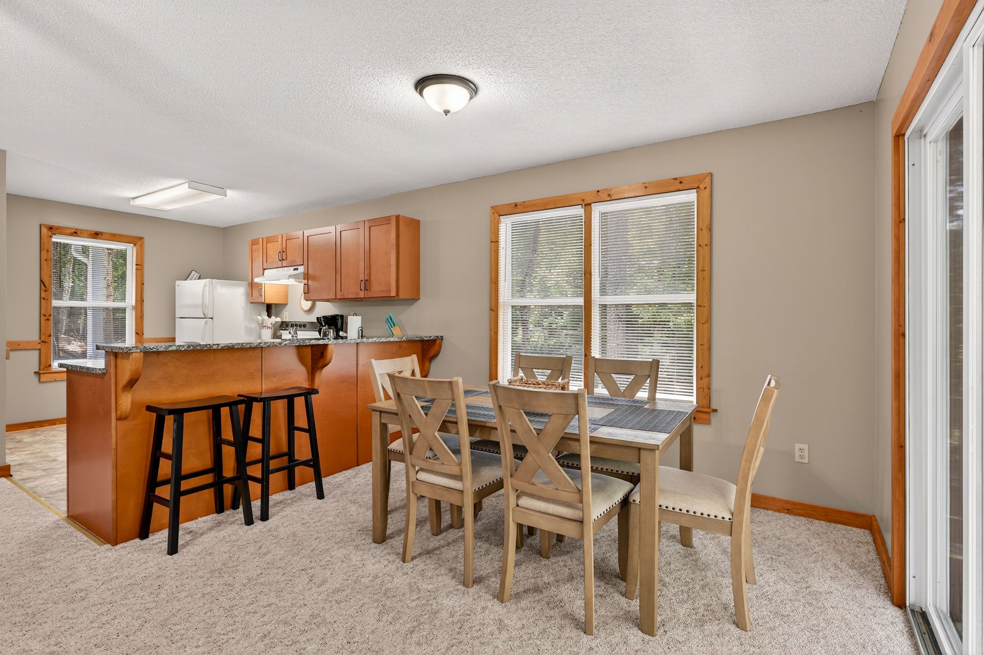Cozy kitchen with dining table, breakfast bar, and light wood cabinets. Beige walls, white appliances, and carpet.