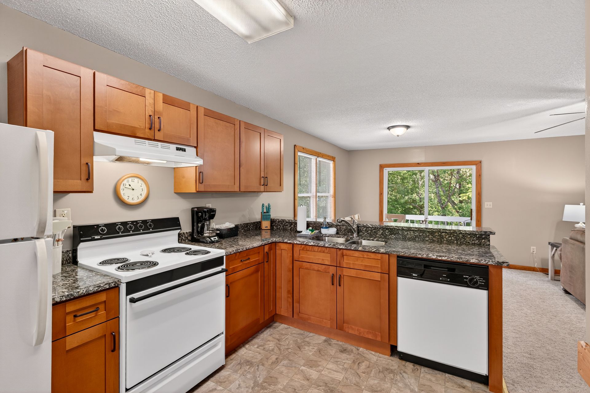 Kitchen with wood cabinets, white appliances, granite countertops, and a window overlooking trees.