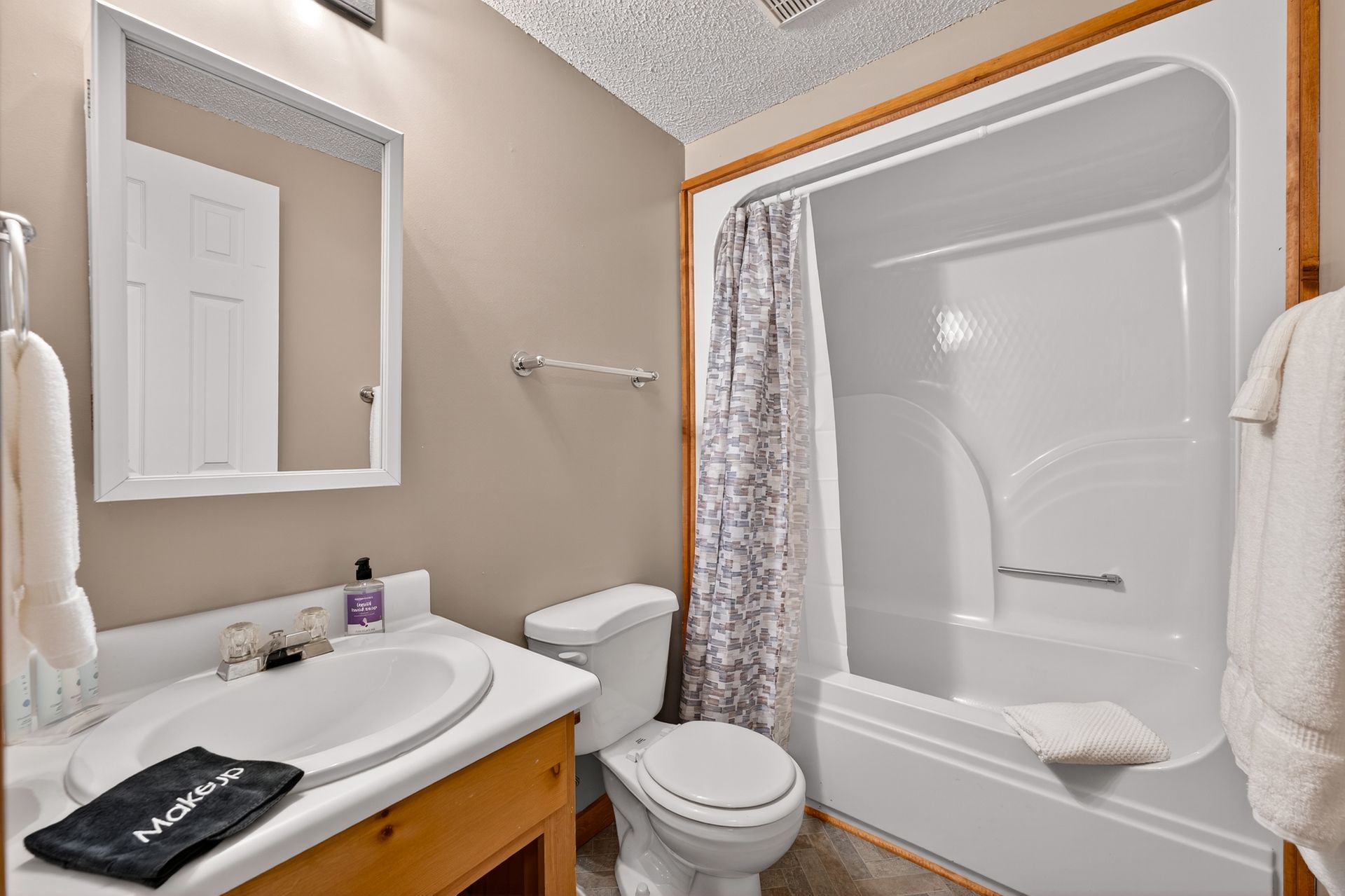 Bathroom with a white tub and toilet, a wooden vanity, and a framed mirror.