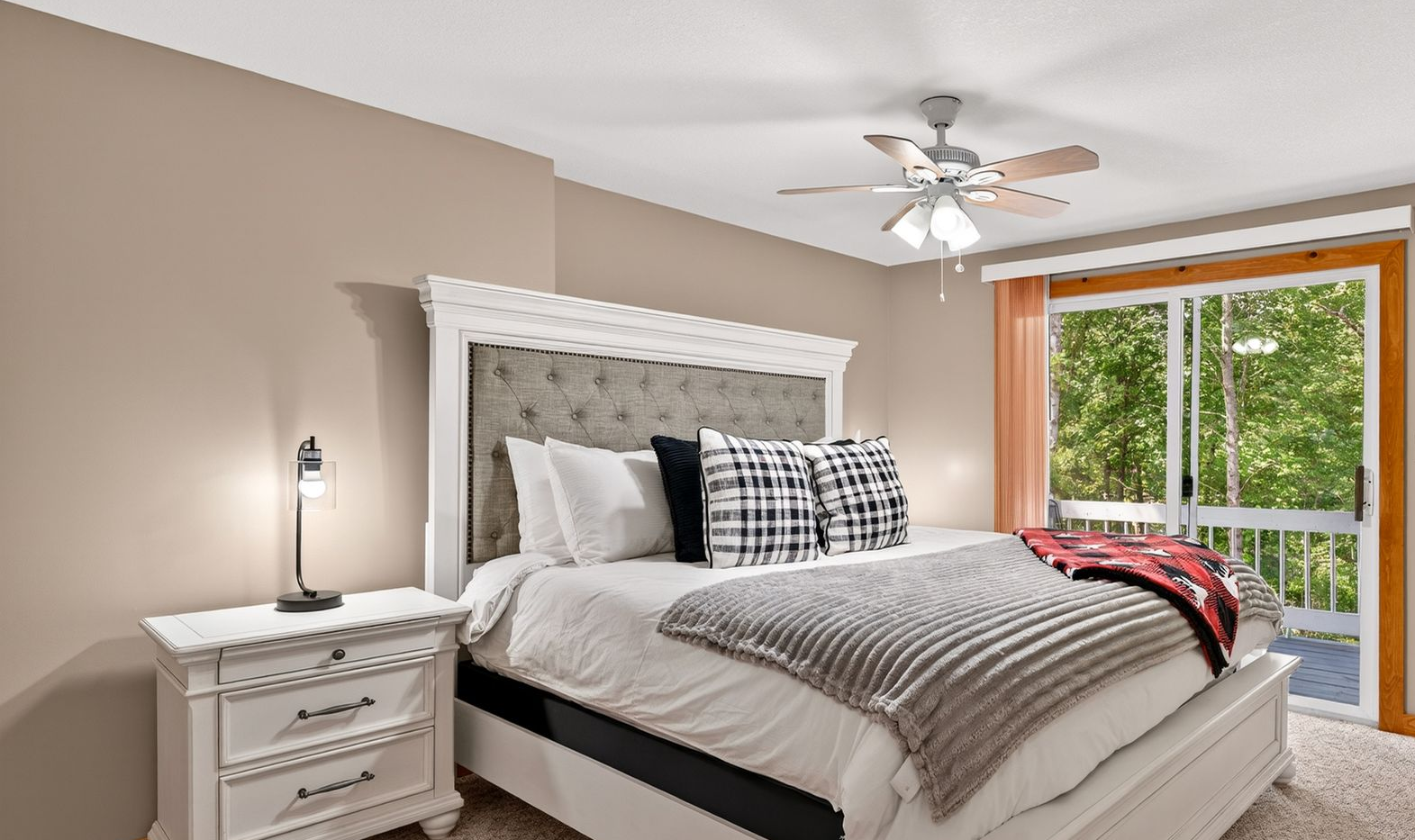 Bedroom with a white bed, nightstand, and a sliding door to a balcony overlooking trees.