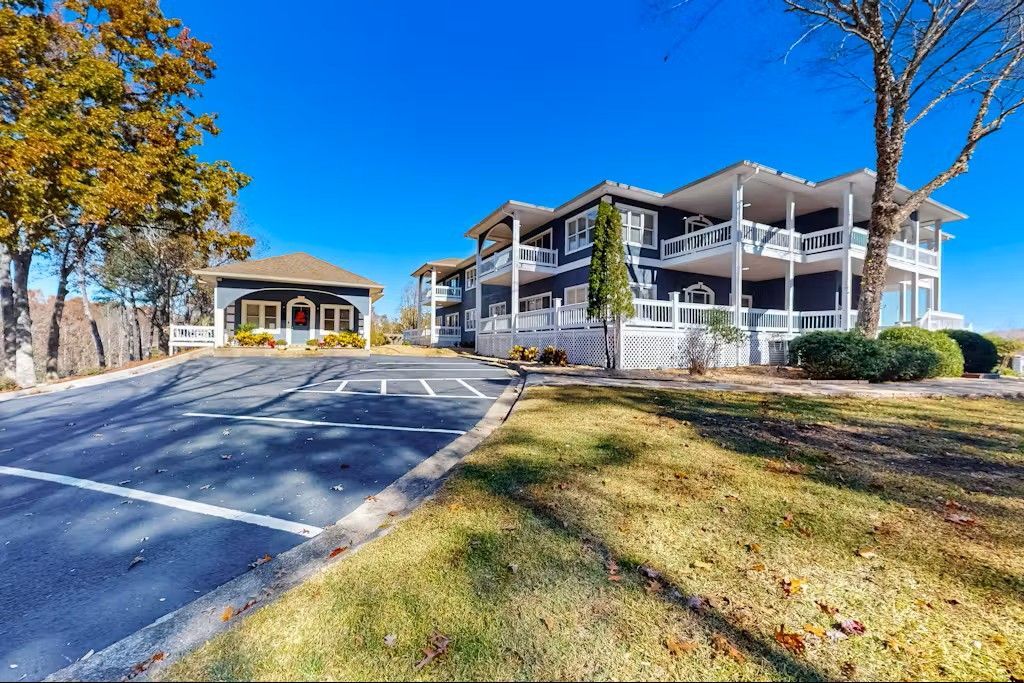Two-story white house with multiple balconies, next to smaller brown building, on a bright, sunny day.