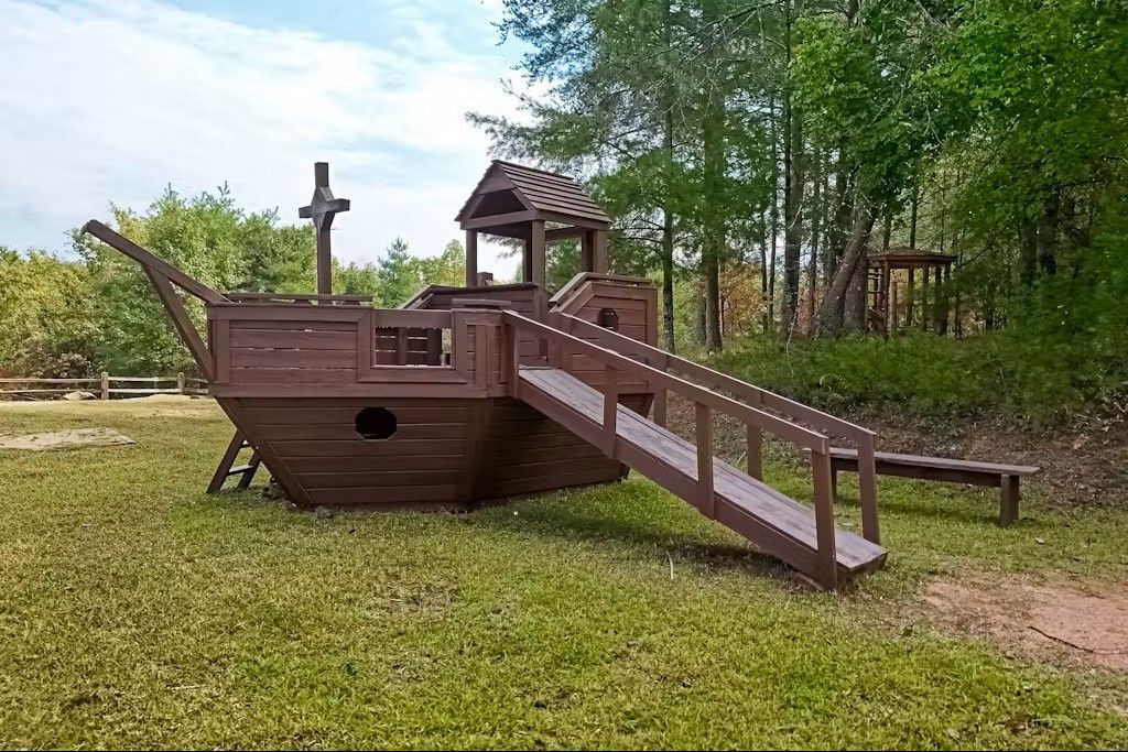 Wooden pirate ship playground on green grass, with a small lookout and slide.