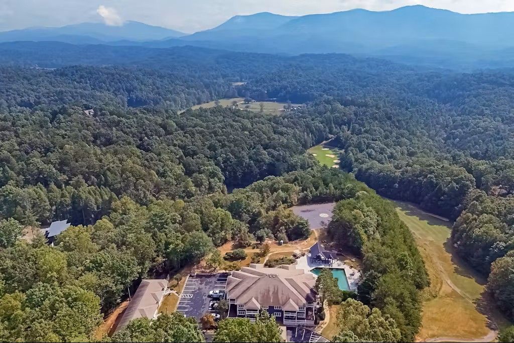 Aerial view of a large building with a pool surrounded by forest and mountains.