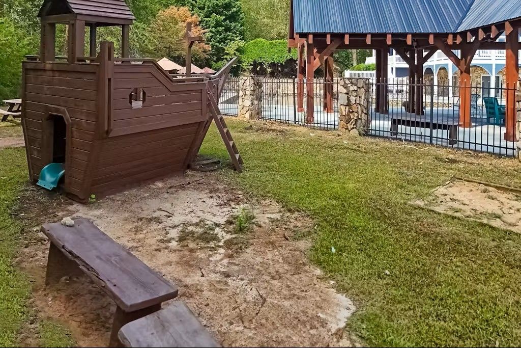Playground with wooden ship structure, bench, and gazebo in yard.