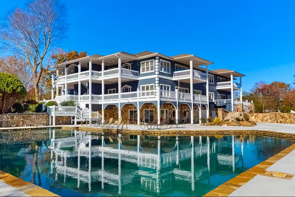 Large, multi-story blue house with white trim reflected in a swimming pool.