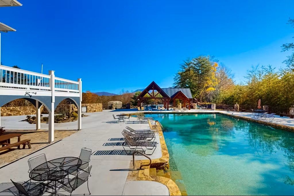 Poolside view with blue sky, outdoor tables, pool, and wooden gazebo in the distance.