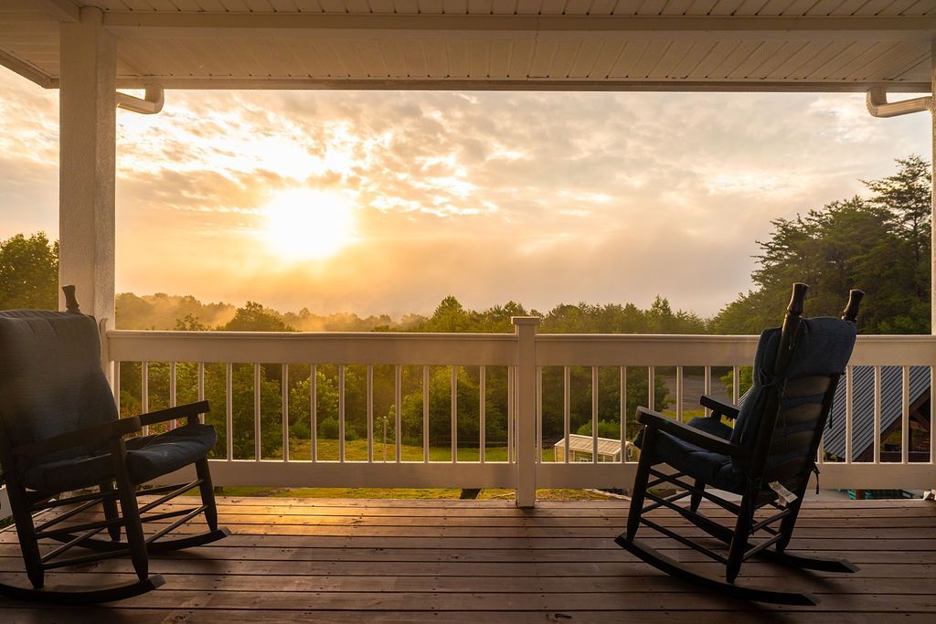 Two rocking chairs on a porch overlooking a misty sunrise over trees.