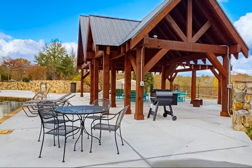 Outdoor pavilion with a grill, table, and chairs. Blue sky.
