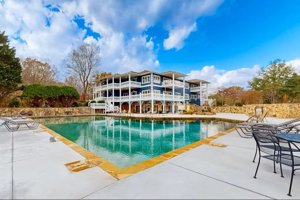 Swimming pool in front of a large blue and white building under a bright blue sky with clouds.