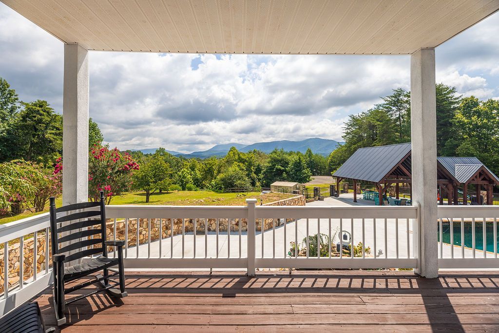 A porch with a rocking chair overlooking a scenic outdoor view of a lush green field and mountains.
