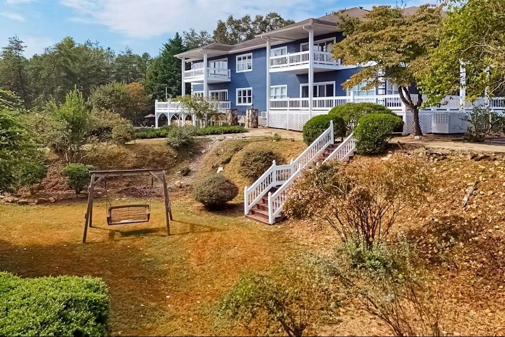 Blue house with balconies on a hill, white railings, steps, swing set in foreground, trees.