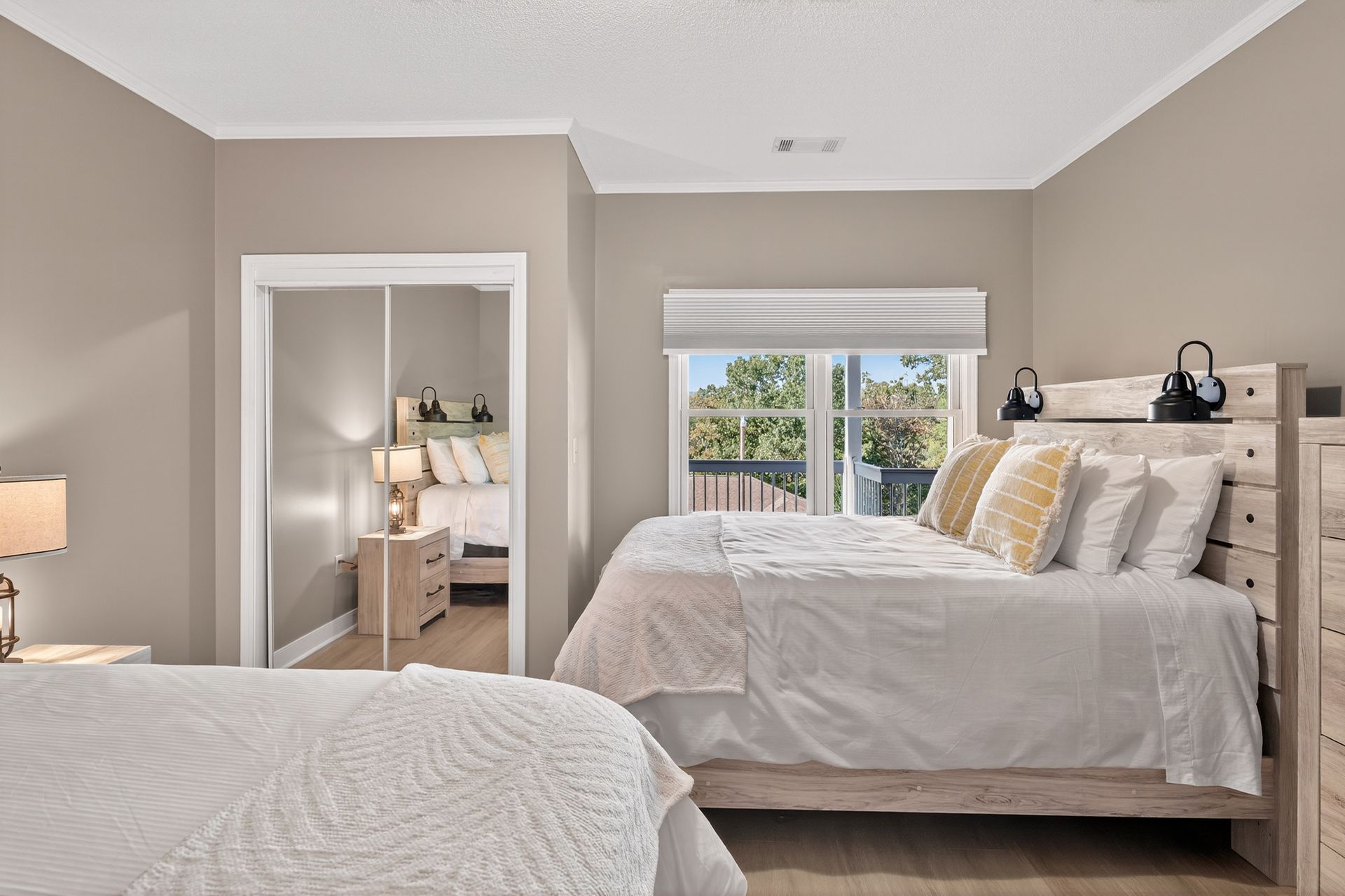 Bedroom with two beds, neutral walls, mirrored closet, and window with outdoor view.