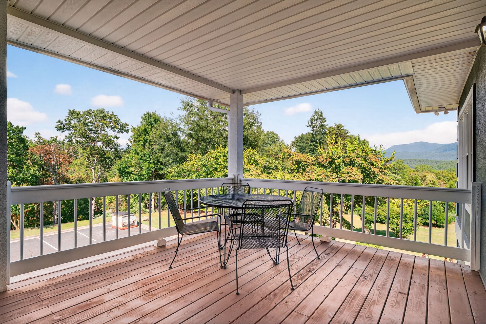 Deck with metal table and chairs overlooking trees and a road; a mountain in the distance.