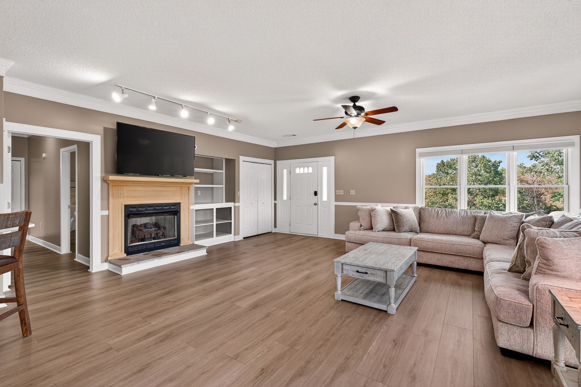 Living room: fireplace with TV, beige sectional sofa, hardwood floors, large windows.
