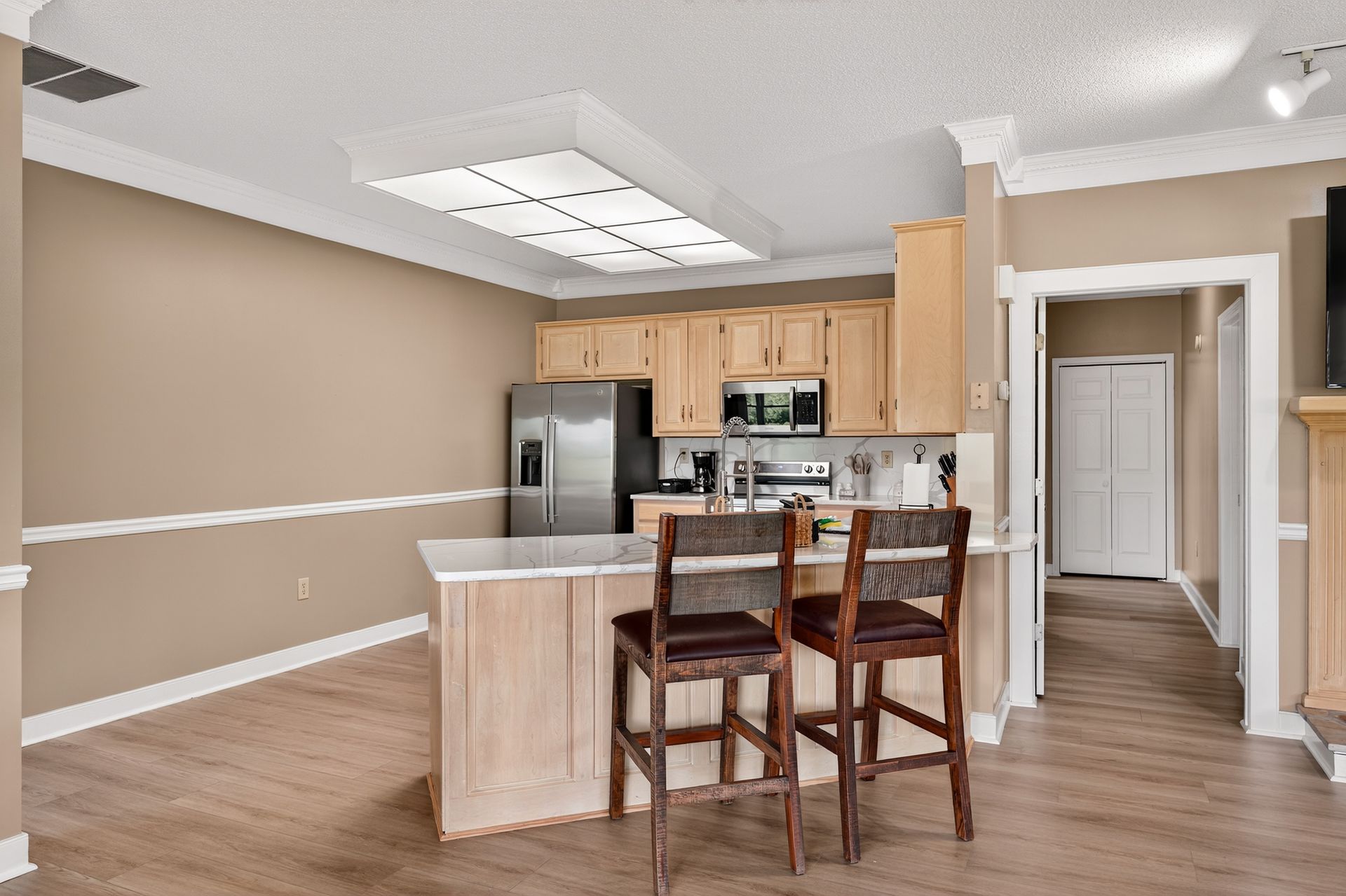 Kitchen with light wood cabinets, stainless steel appliances, island with stools, and neutral-toned walls.