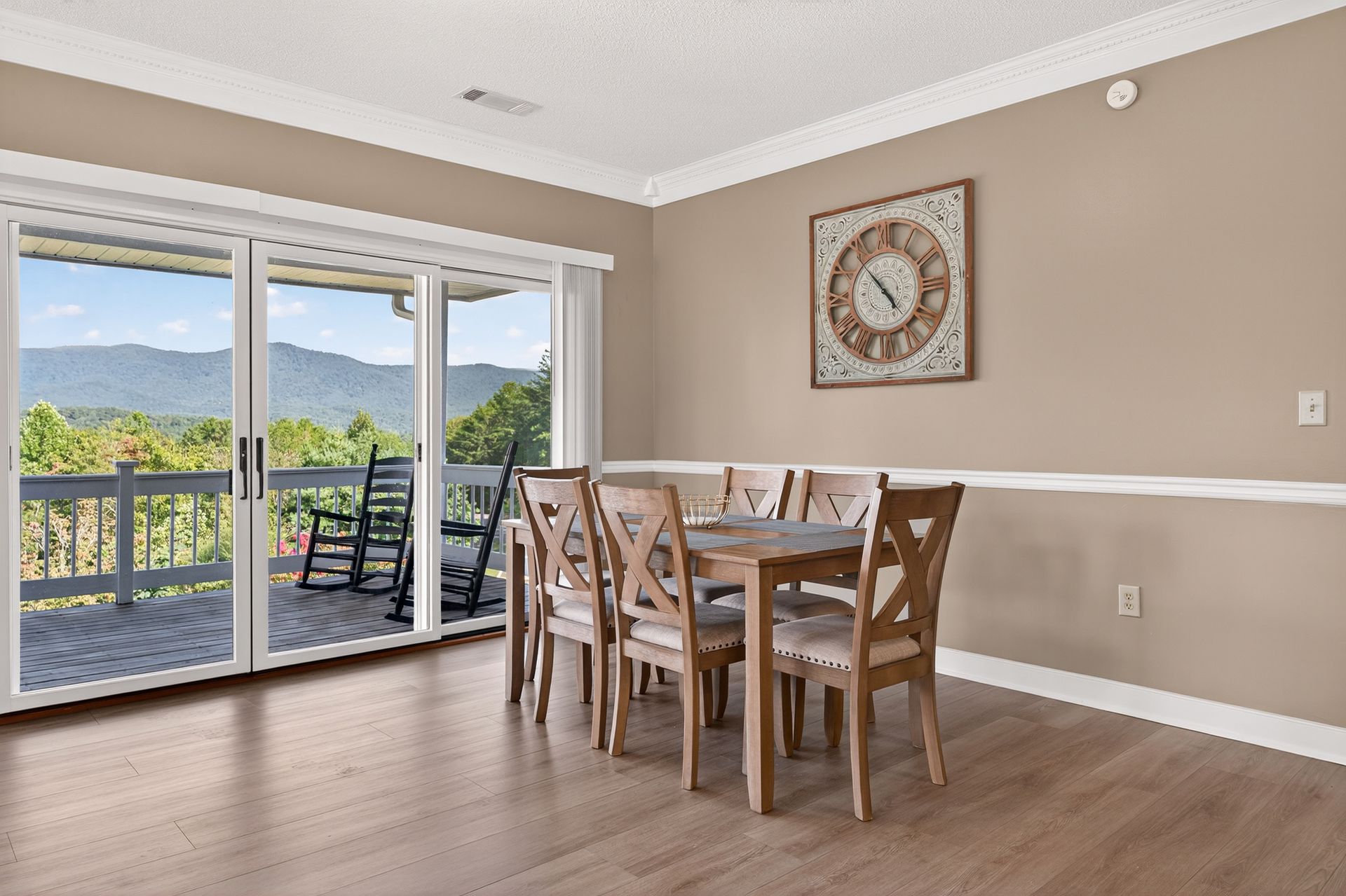 Dining room with table, chairs, large windows overlooking a mountain view. Clock on wall.