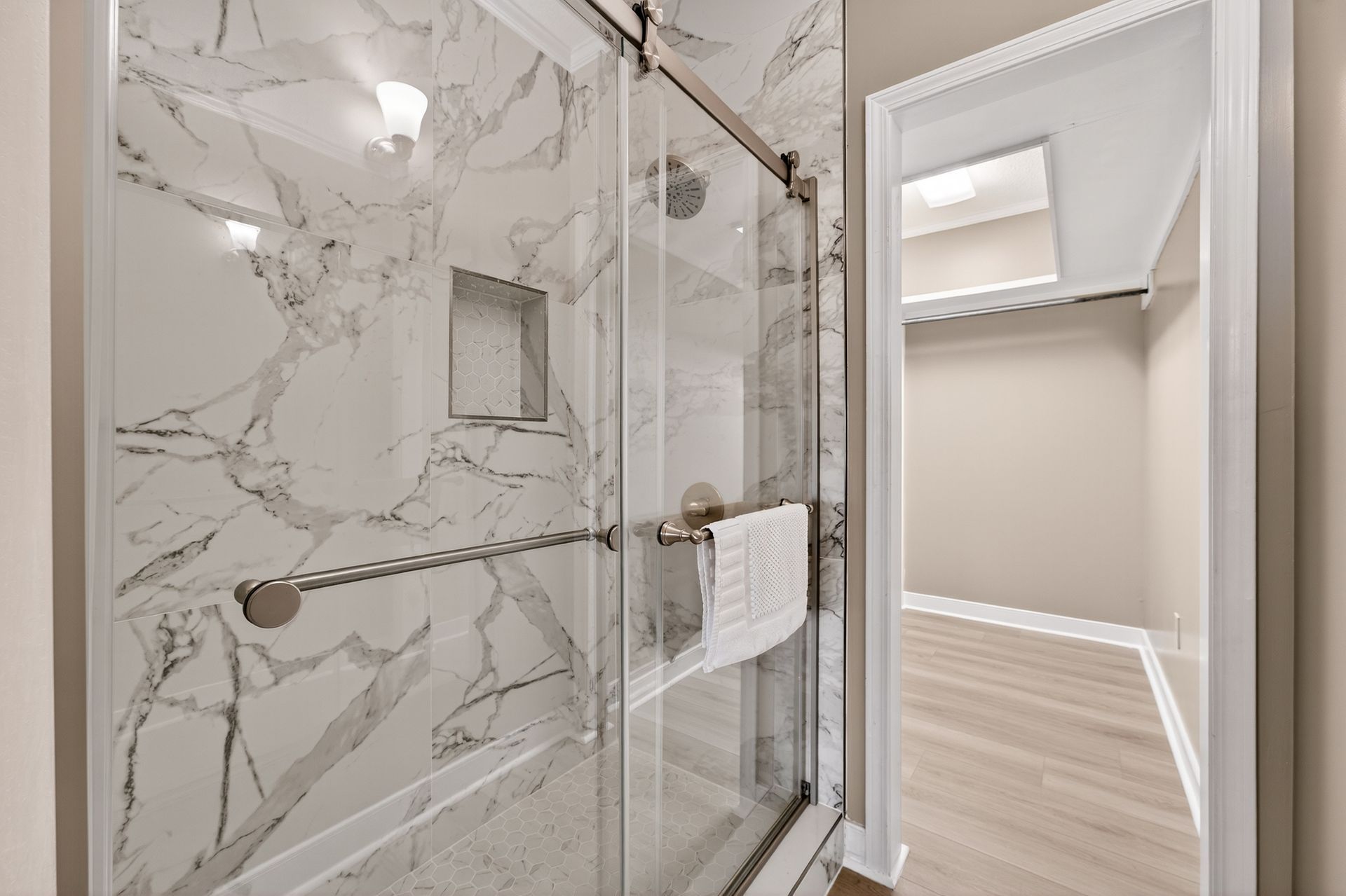 Bathroom with marble tile shower, glass door, and walk-in closet in the background.