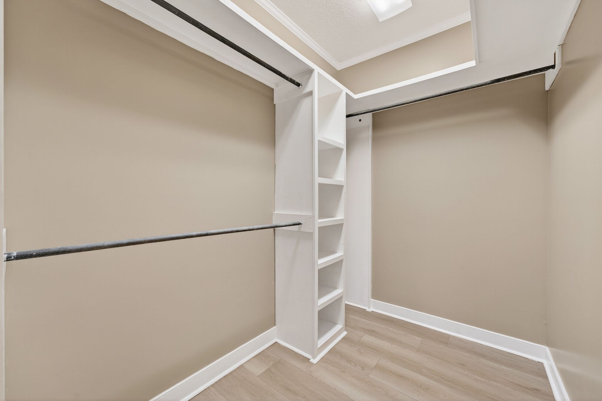 Empty walk-in closet with beige walls, white shelves, and a rod for hanging clothes.
