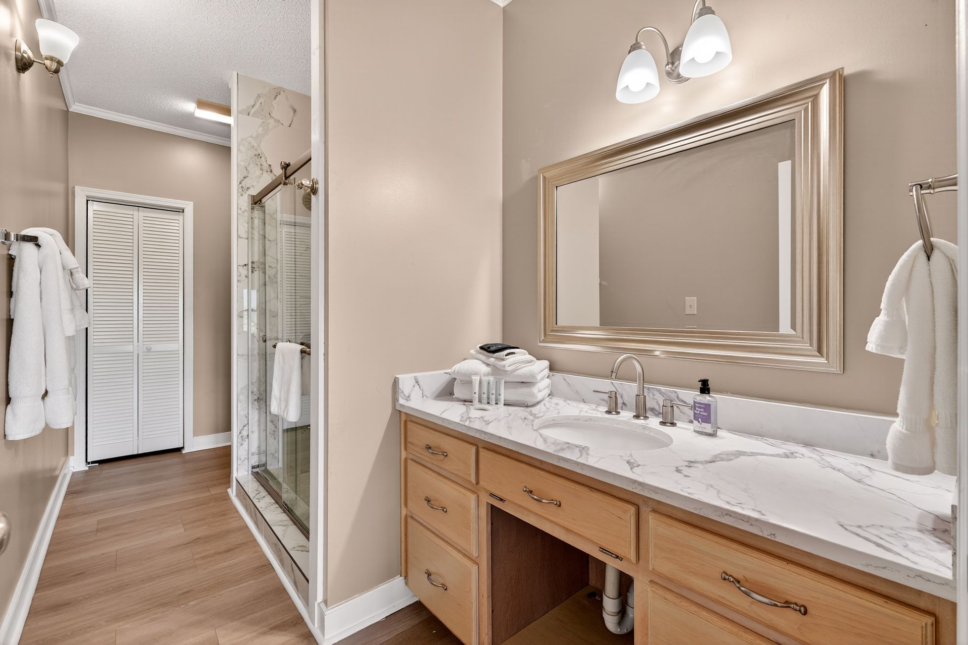 Bathroom with vanity, mirror, shower, and towels. Beige walls, wood cabinets, and marble-look countertop.