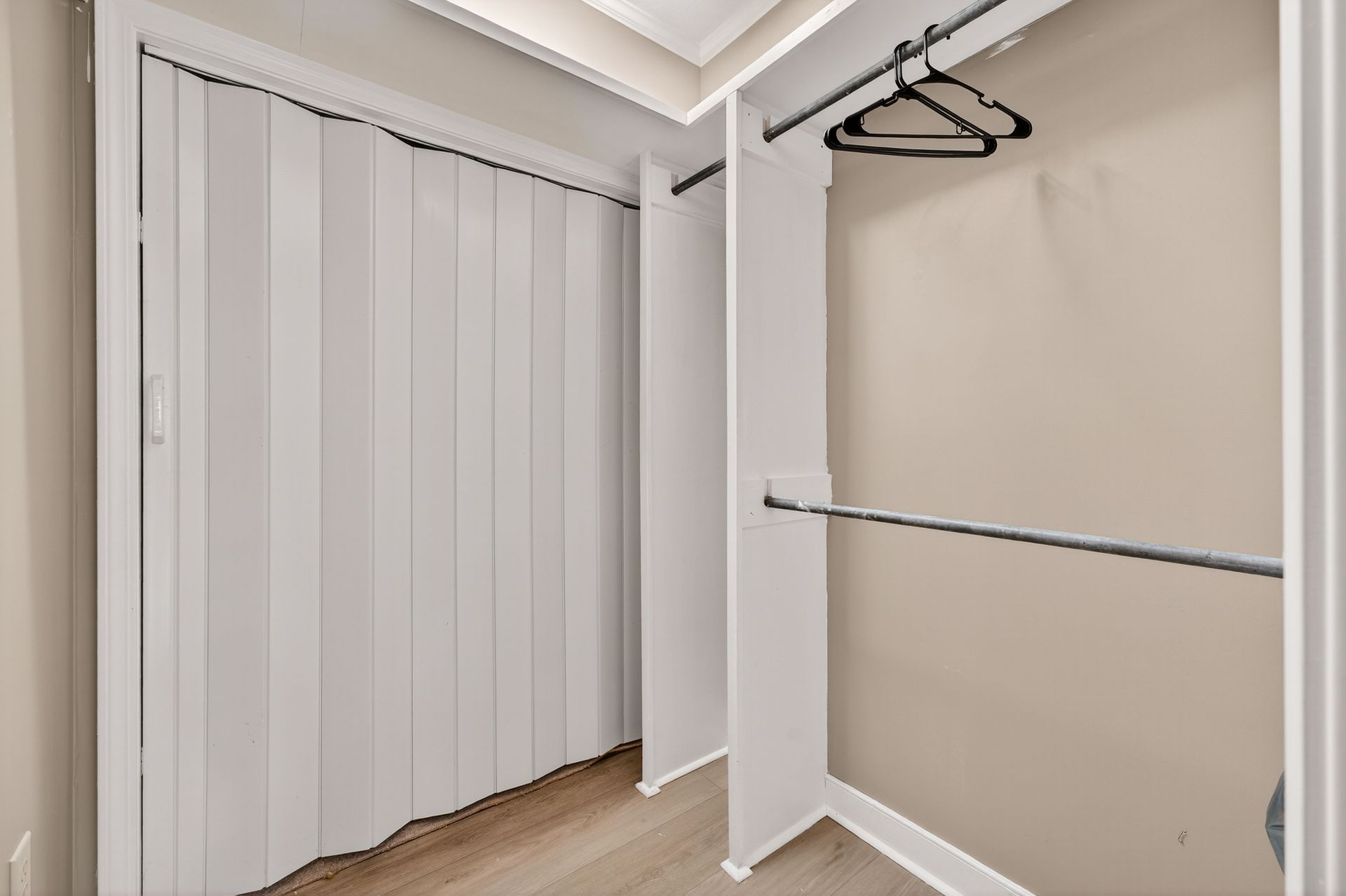 Empty white closet with accordion doors and hanging rods.