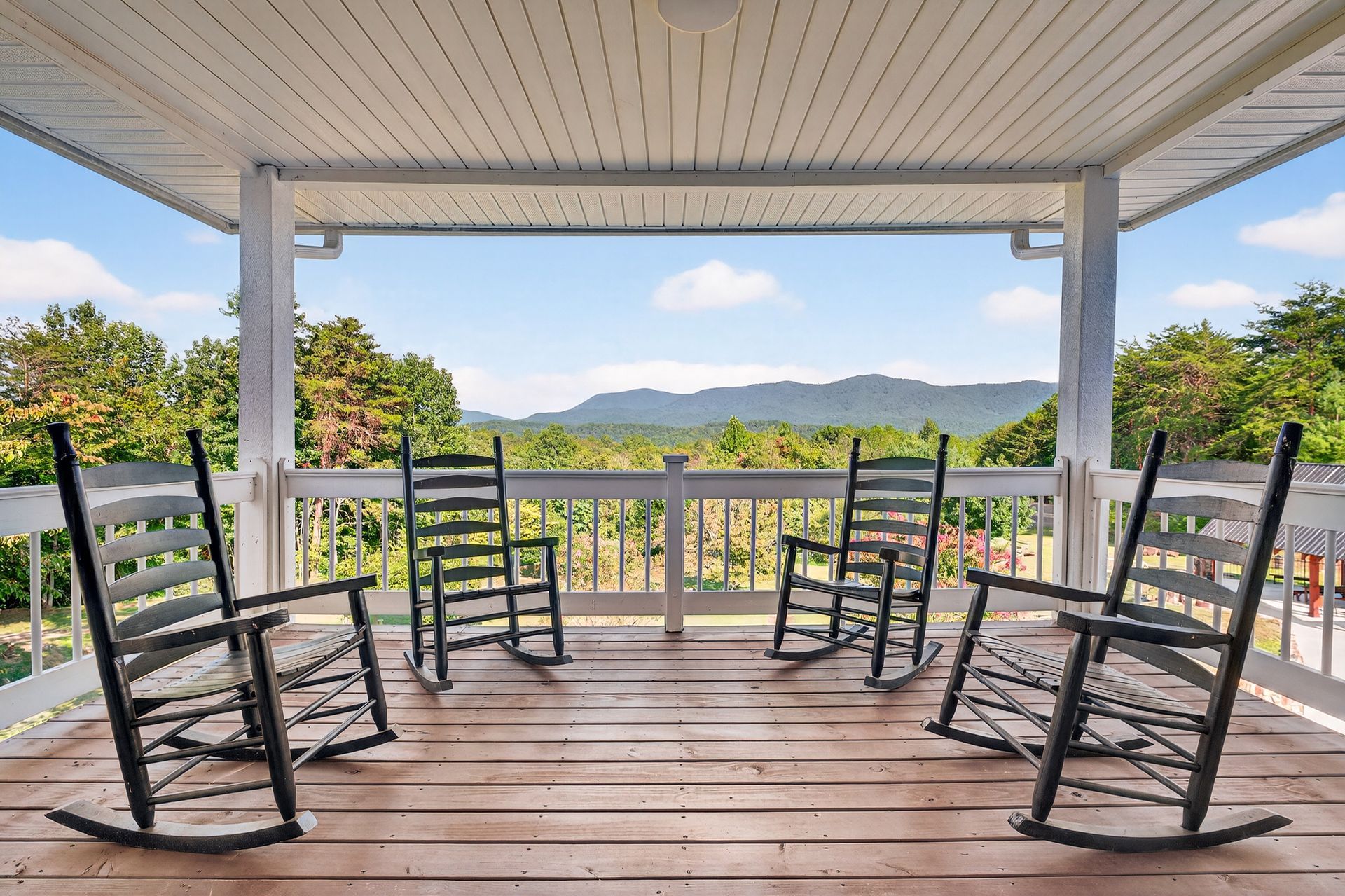 Wooden rocking chairs on a porch overlooking a mountain range on a sunny day.
