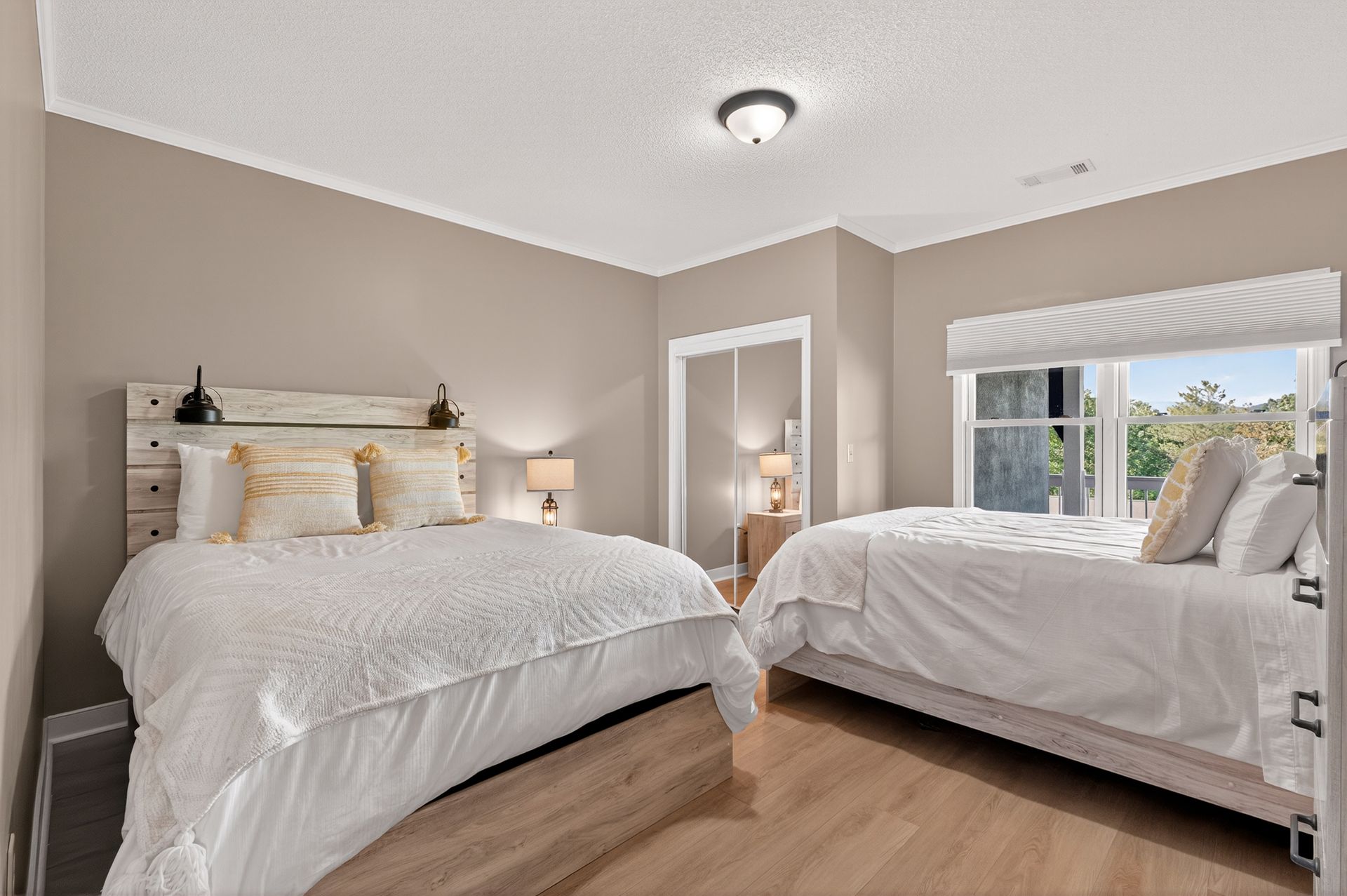 Bedroom with two beds, neutral walls, natural light, light wood floors.