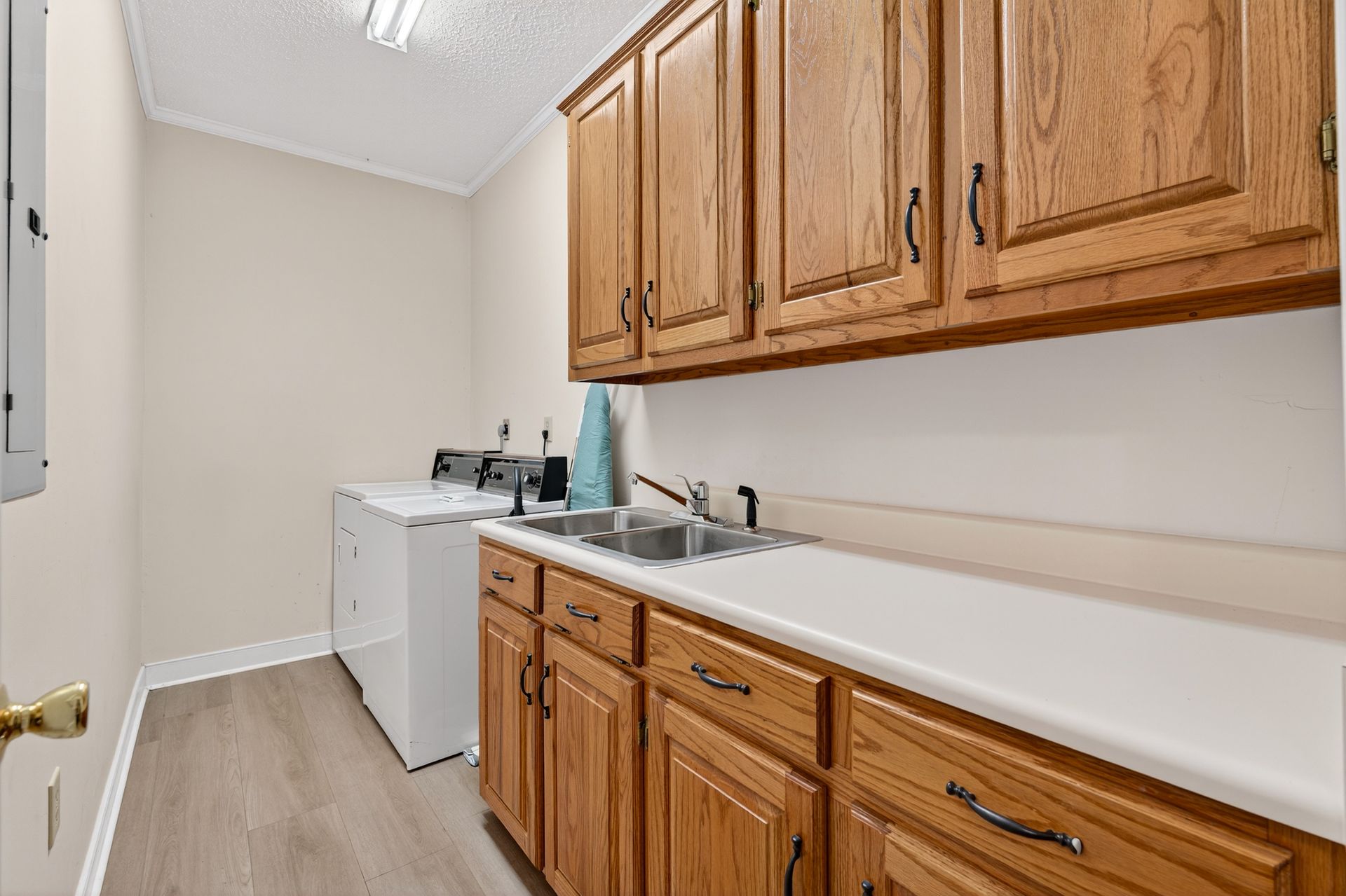 Laundry room with light-colored cabinets and countertop, a sink, a washing machine, and light flooring.