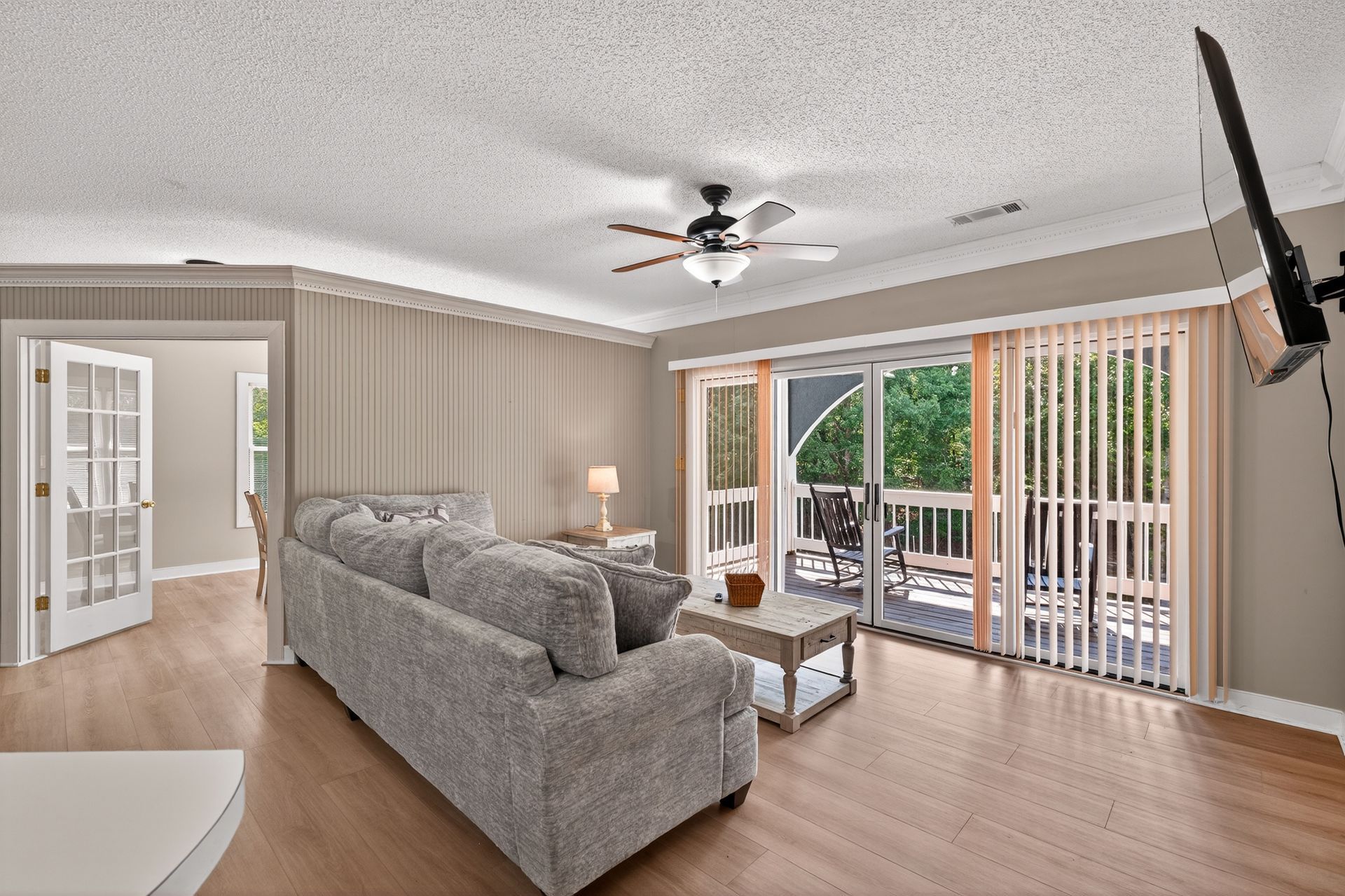 Living room with gray couch, sliding door to balcony, vertical blinds, and mounted TV.