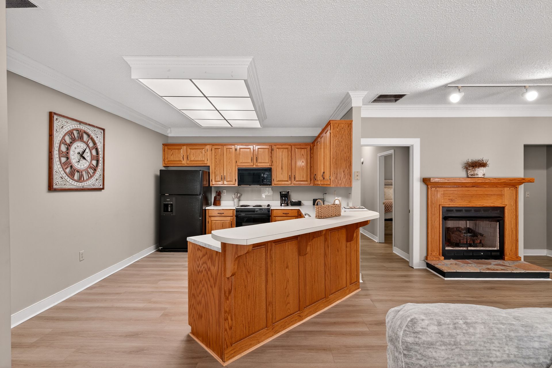 Kitchen with wooden cabinets, black appliances, and a white countertop. A fireplace is to the right.