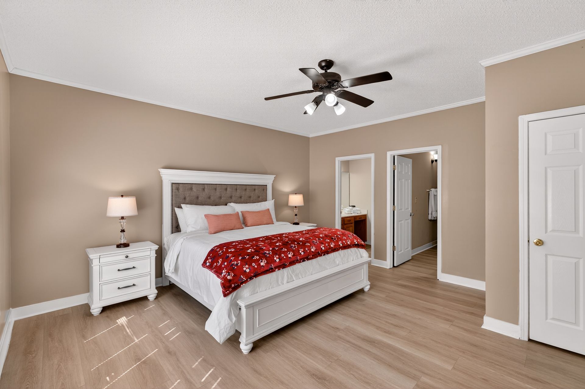 Bedroom with a white bed, tan walls, and hardwood floors; features a ceiling fan.