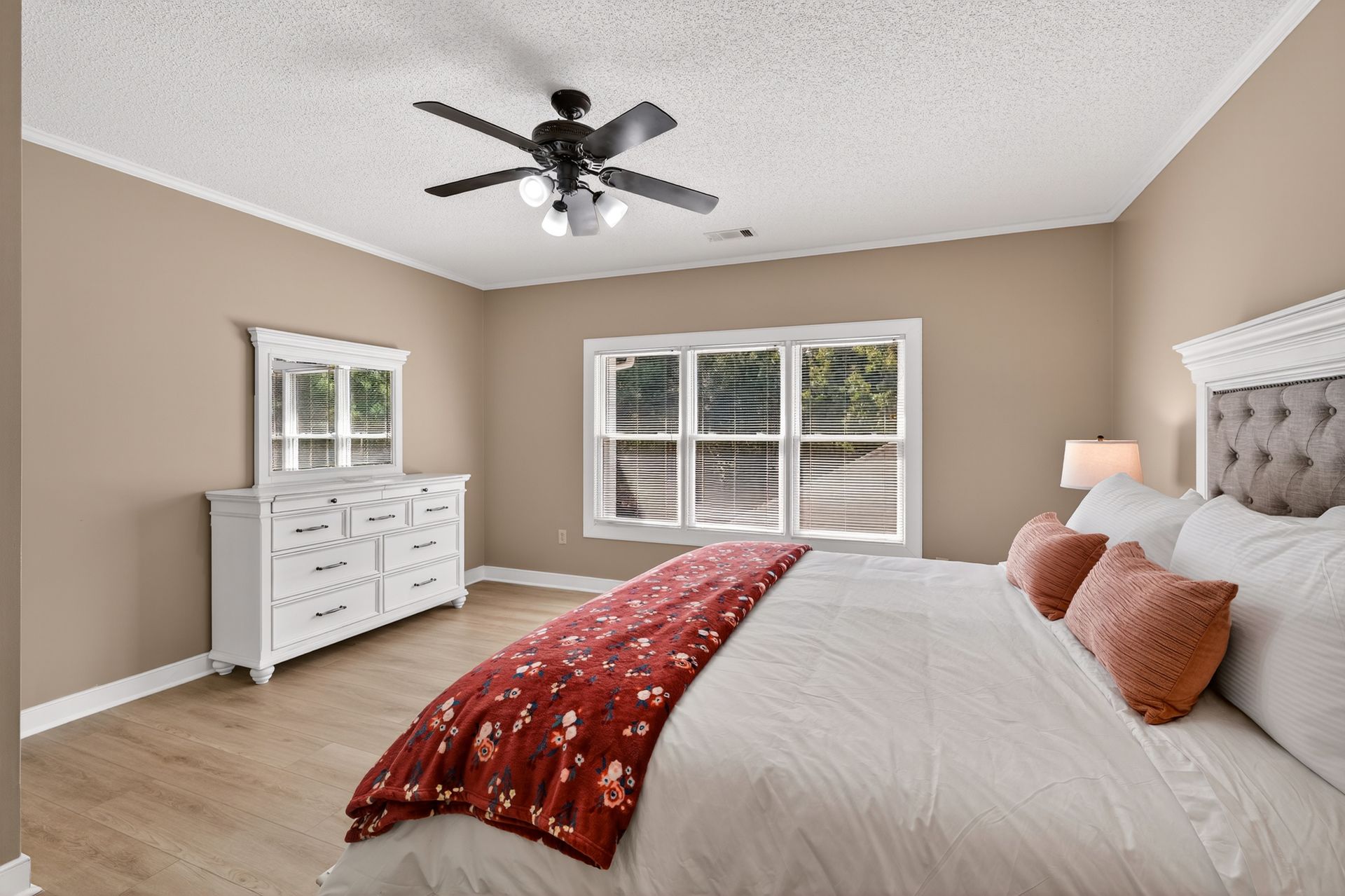 Bedroom with white furniture, tan walls, and a red floral blanket.