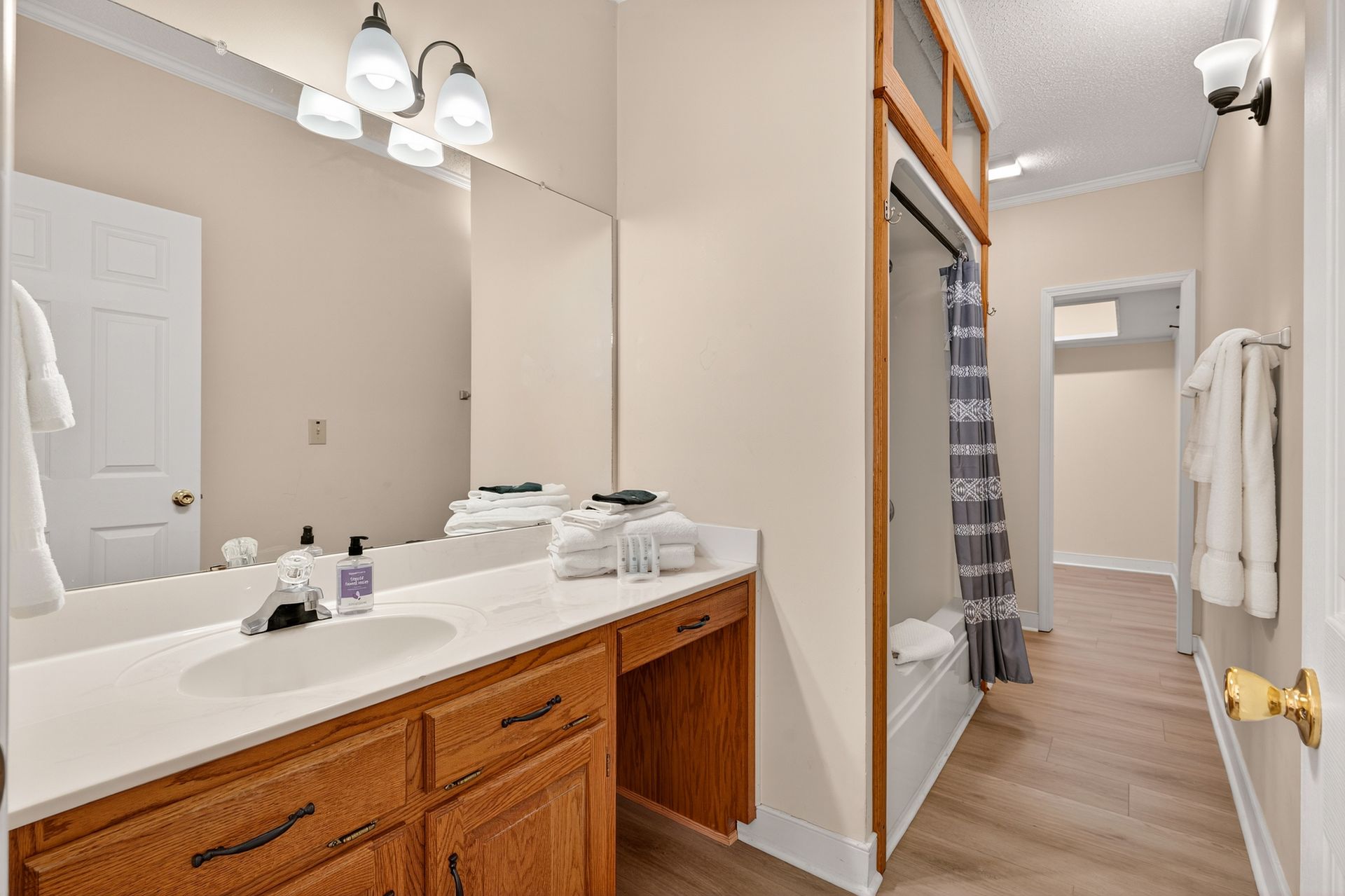 Bathroom with light-wood vanity, large mirror, and walk-in closet. Off-white walls and light-colored flooring.