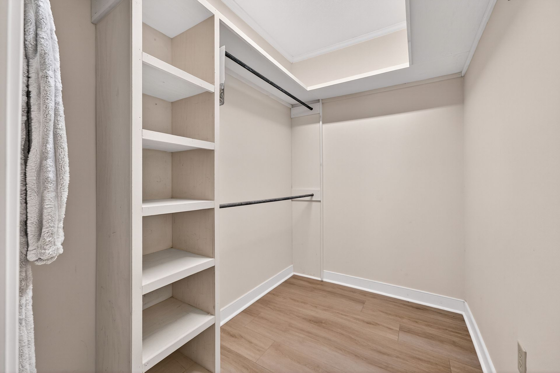 Empty walk-in closet with built-in shelves on one side, a hanging rod, and light wood floors.