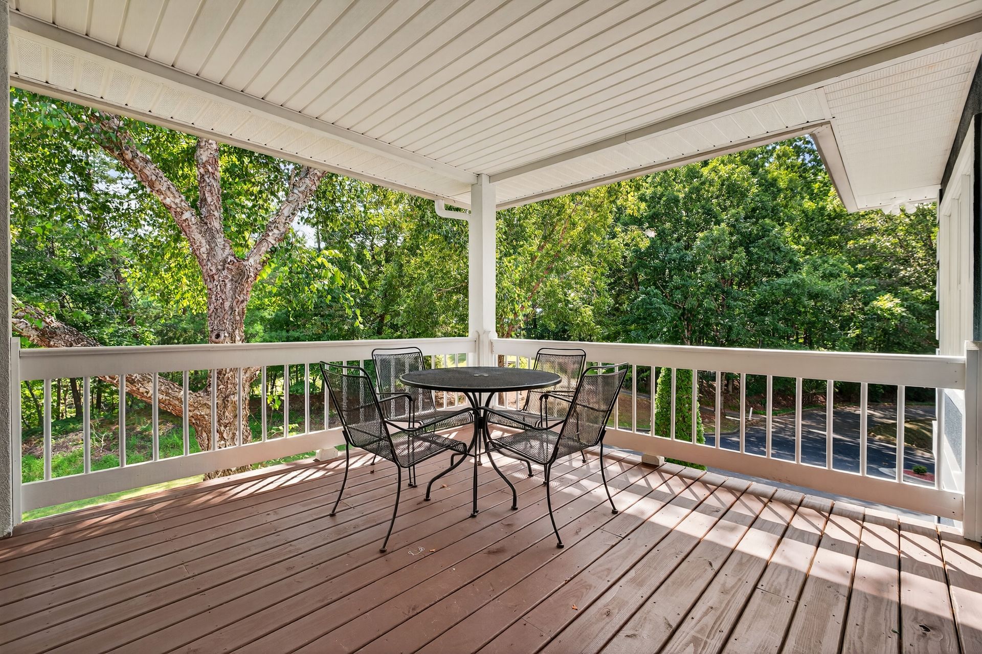 Wooden porch with table and chairs, surrounded by lush green trees.