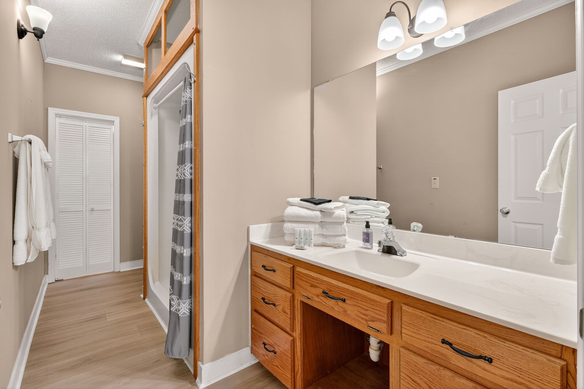 Bathroom with wood cabinets, white countertop, large mirror, shower, and stacked white towels.