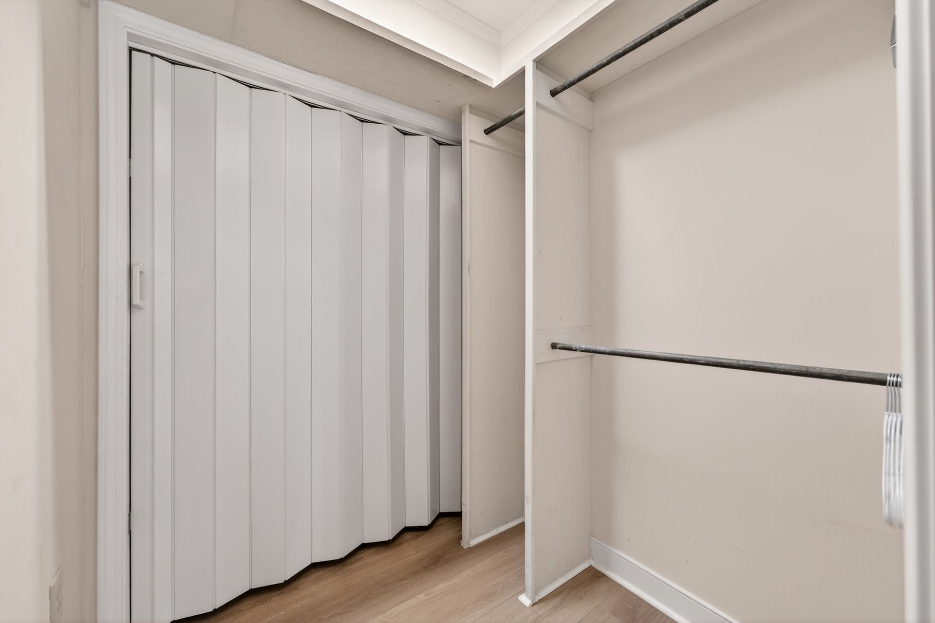 Walk-in closet with accordion door, shelving, and a hanging rod.