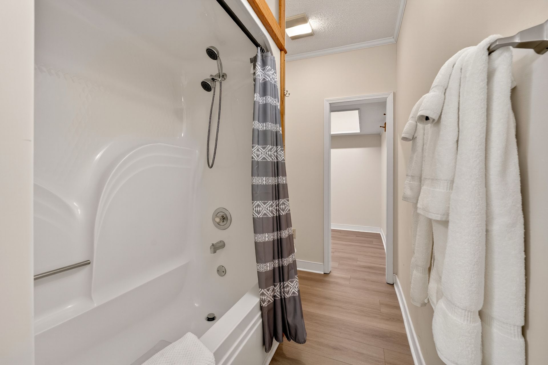 Bathroom: shower with gray curtain, white towels, hallway with wooden floor.