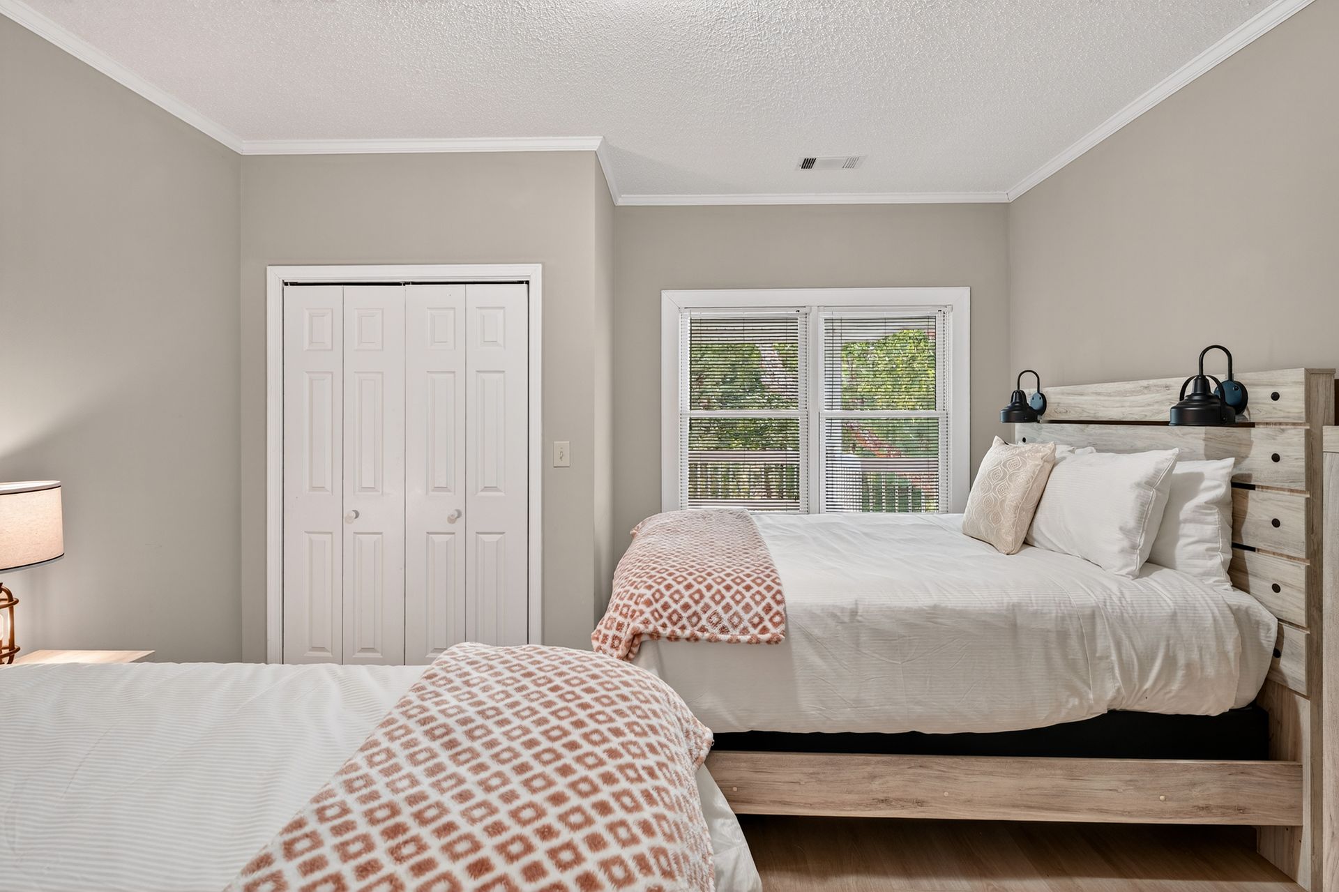 Bedroom with two white beds, window, closed closet, and neutral walls.