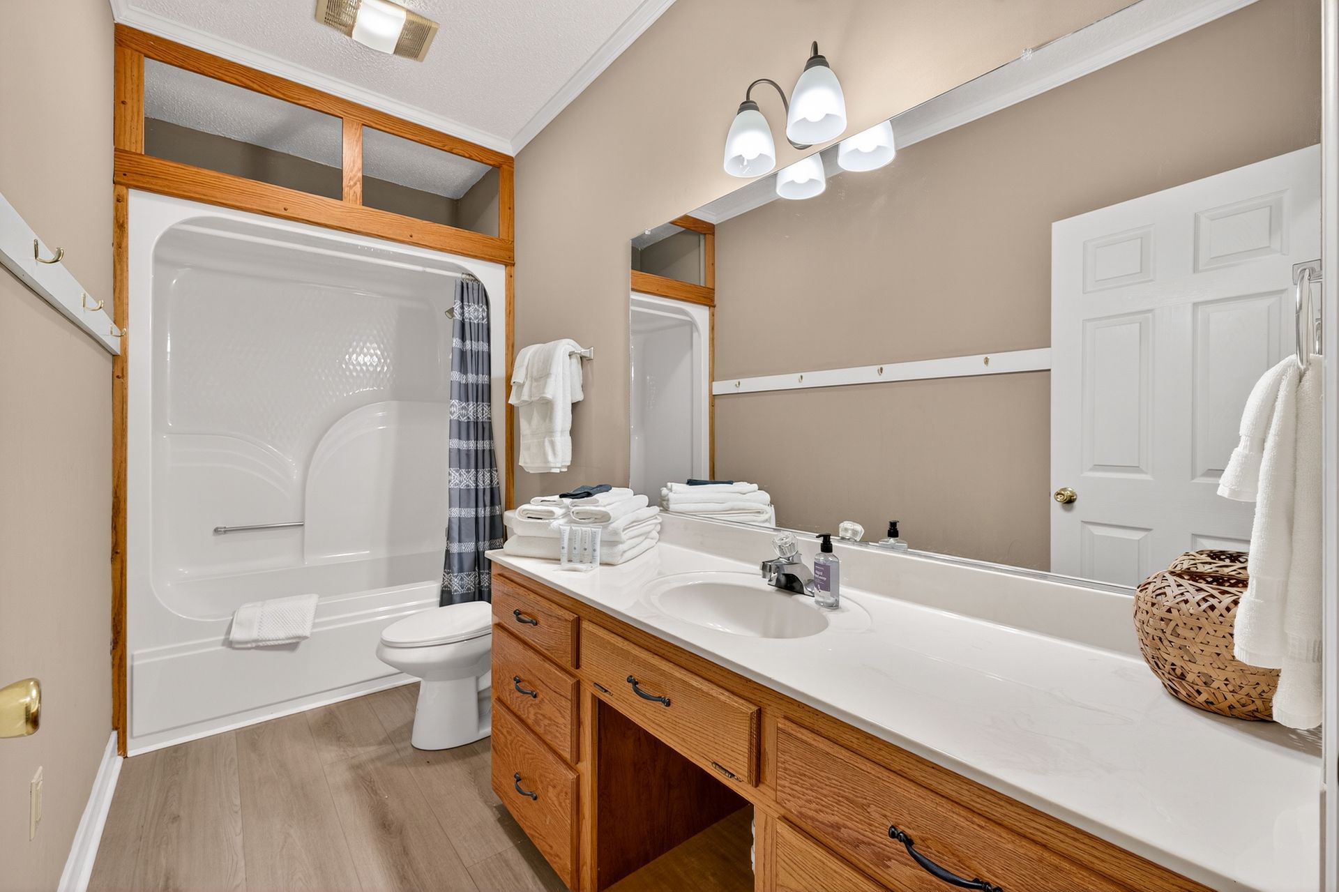 Bathroom with white countertops, wooden cabinets, beige walls, and a white shower/tub.