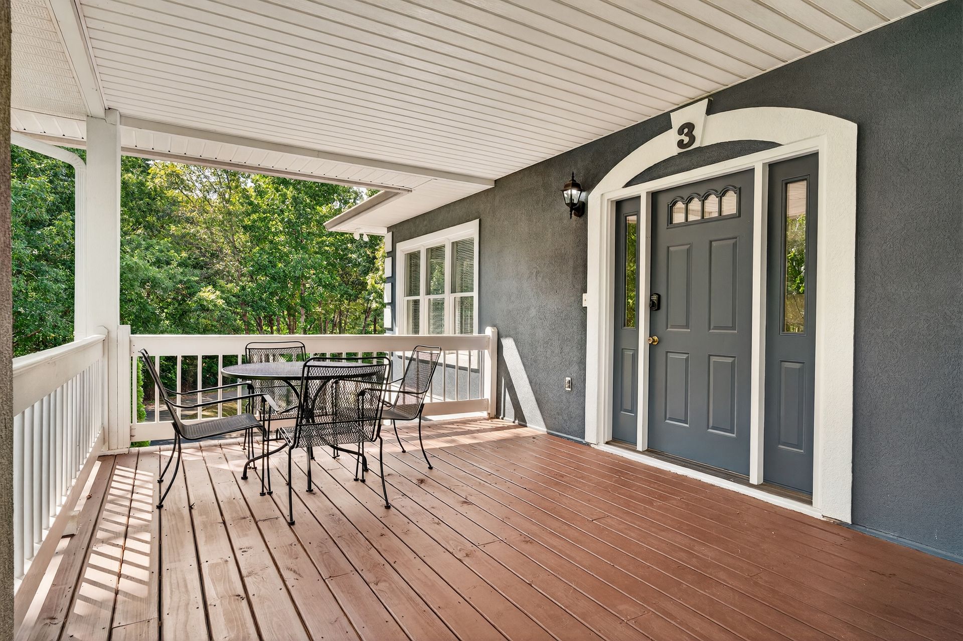 Covered porch with dark gray door, round table and chairs; number 3 above door.