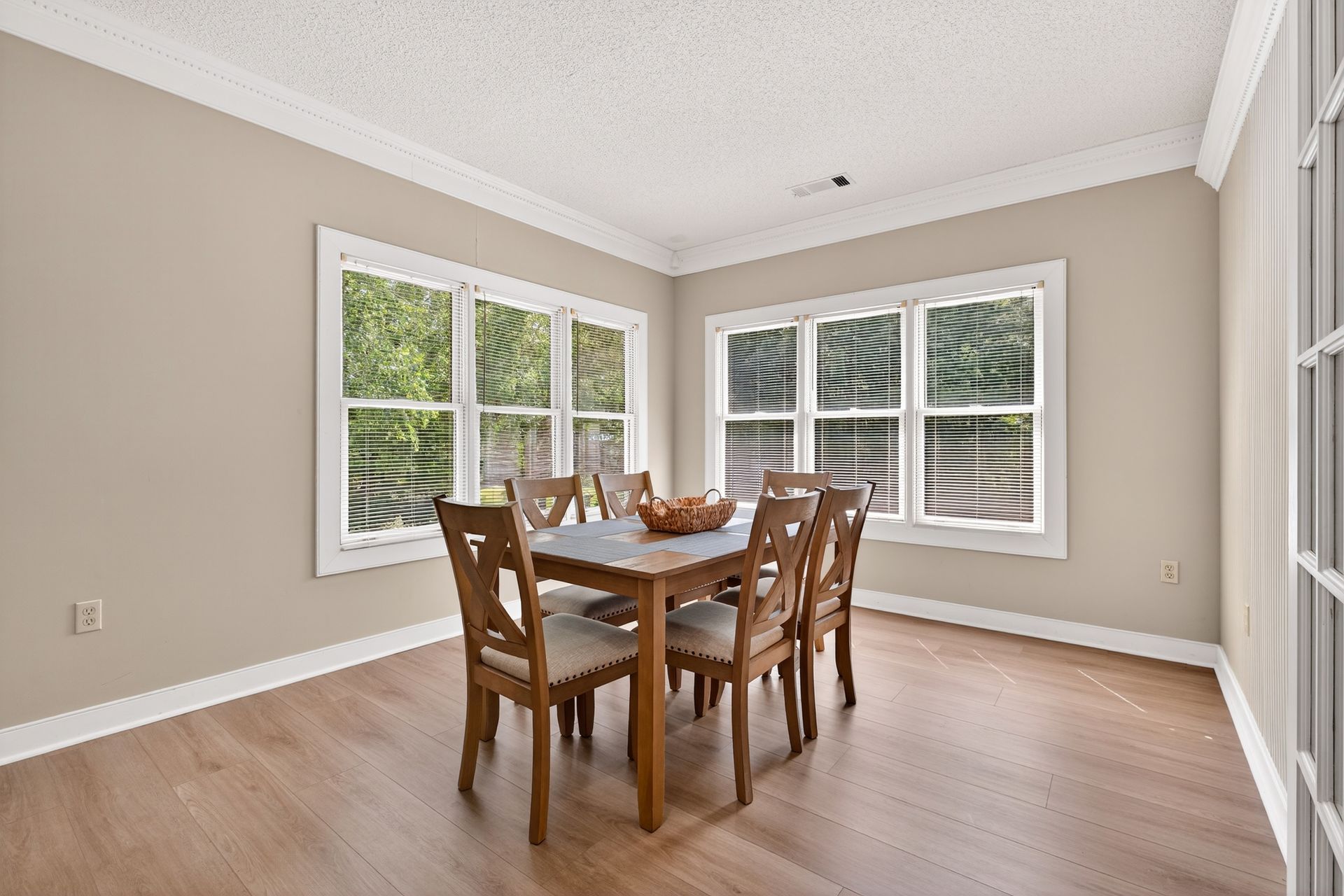 Dining room with wooden table and chairs, two windows, beige walls, and wood flooring.
